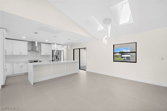 kitchen with white cabinets, wall chimney exhaust hood, light tile patterned floors, and an island with sink