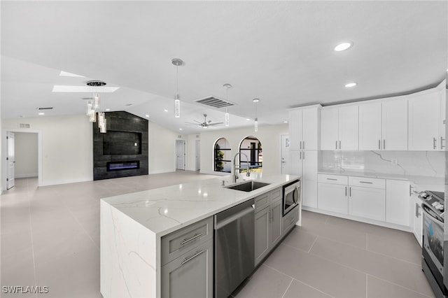 kitchen featuring white cabinets, stainless steel appliances, hanging light fixtures, and a center island with sink