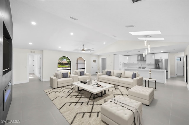 living room featuring ceiling fan, vaulted ceiling with skylight, and light tile patterned flooring