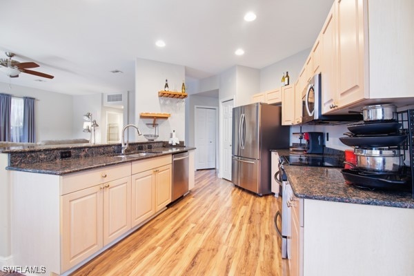 kitchen featuring ceiling fan, sink, stainless steel appliances, dark stone counters, and light wood-type flooring