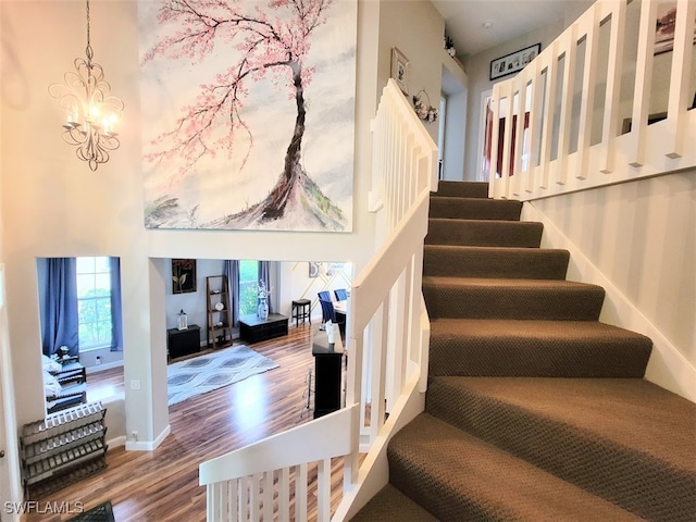 staircase with hardwood / wood-style floors, a high ceiling, and an inviting chandelier