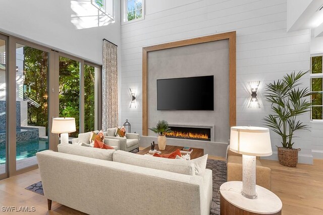 living room featuring plenty of natural light, wood finished floors, a lit fireplace, wood walls, and a towering ceiling