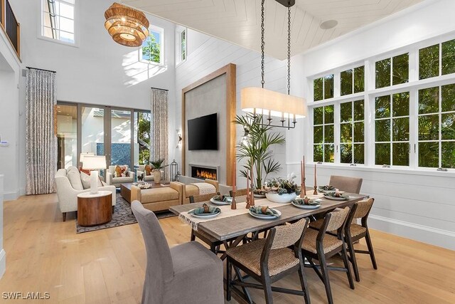 dining area featuring a high ceiling, light wood finished floors, a lit fireplace, and baseboards