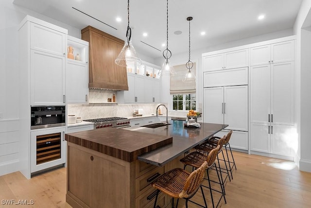 kitchen featuring a sink, wine cooler, an island with sink, backsplash, and a kitchen breakfast bar