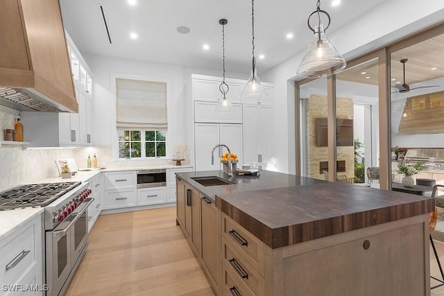 kitchen with a sink, custom range hood, double oven range, backsplash, and a kitchen island with sink