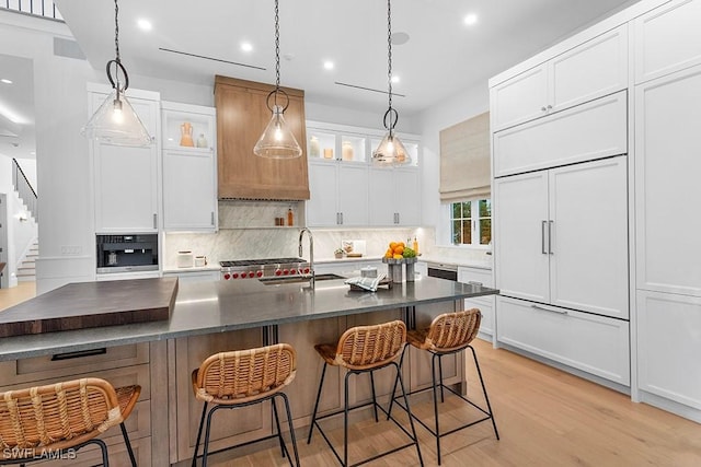 kitchen featuring paneled refrigerator, a sink, tasteful backsplash, dark countertops, and light wood-style flooring