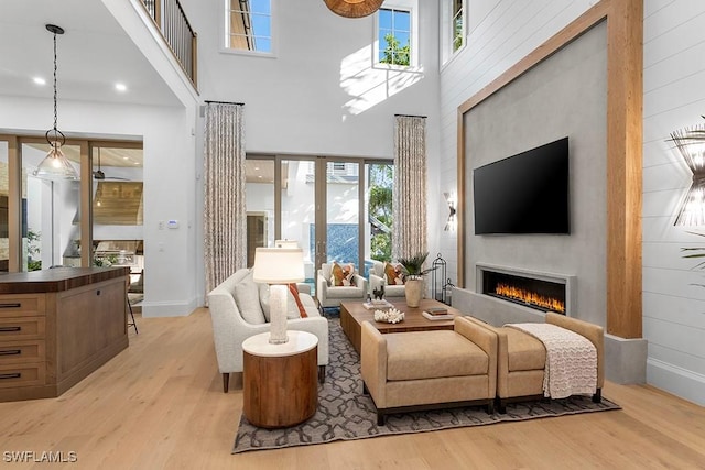 living room featuring light wood-type flooring, a lit fireplace, a high ceiling, and baseboards