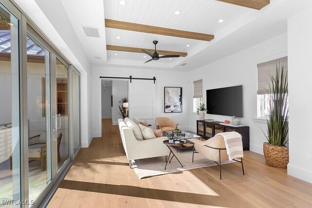 living area with a barn door, light wood-type flooring, baseboards, beam ceiling, and ceiling fan
