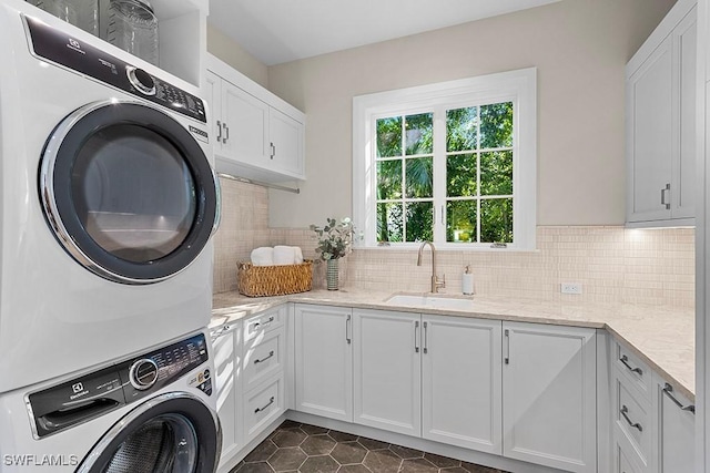 laundry area with estacked washer and dryer, cabinet space, and dark tile patterned flooring