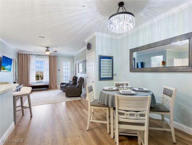 dining area with hardwood / wood-style floors, ceiling fan with notable chandelier, and crown molding