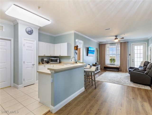 kitchen featuring light hardwood / wood-style floors, kitchen peninsula, ornamental molding, a breakfast bar area, and white cabinets