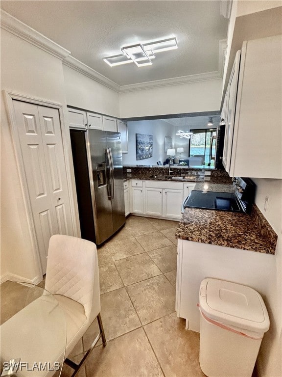 kitchen featuring stainless steel refrigerator with ice dispenser, black range oven, a textured ceiling, crown molding, and white cabinetry