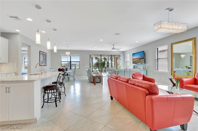 living room featuring ceiling fan with notable chandelier, light tile patterned floors, and sink