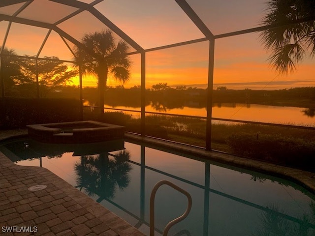 pool at dusk featuring a patio, a water view, a lanai, and an in ground hot tub