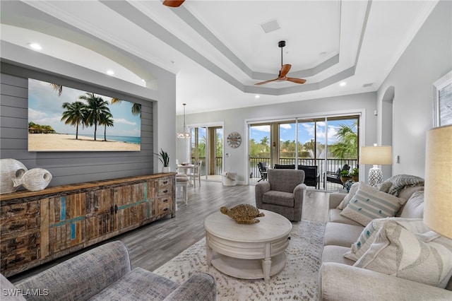 living room with hardwood / wood-style floors, ceiling fan with notable chandelier, a raised ceiling, and crown molding