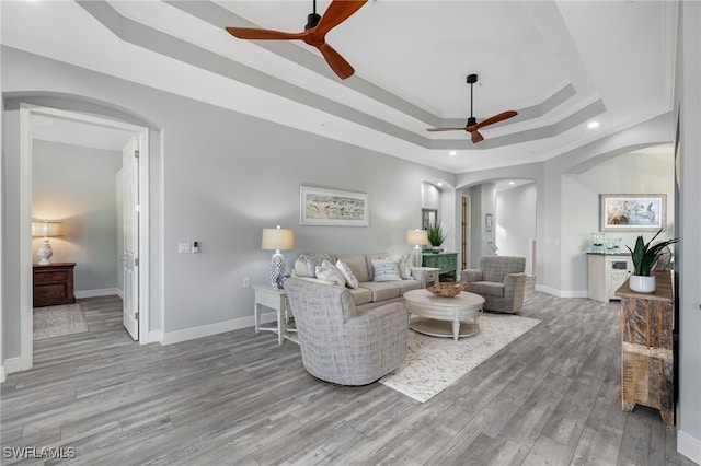 living room featuring hardwood / wood-style floors, ceiling fan, ornamental molding, and a tray ceiling