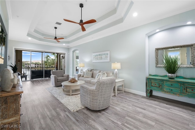 living room featuring light hardwood / wood-style floors, ceiling fan, a raised ceiling, and ornamental molding