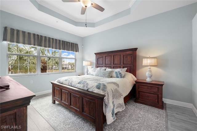 bedroom with ornamental molding, ceiling fan, a tray ceiling, and light hardwood / wood-style floors