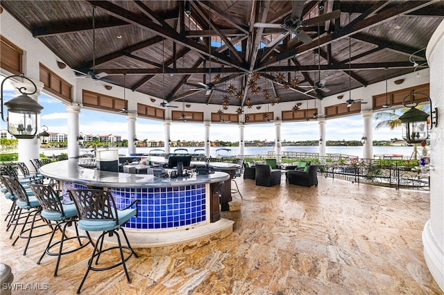 unfurnished sunroom featuring a water view, vaulted ceiling with beams, ceiling fan, and wooden ceiling