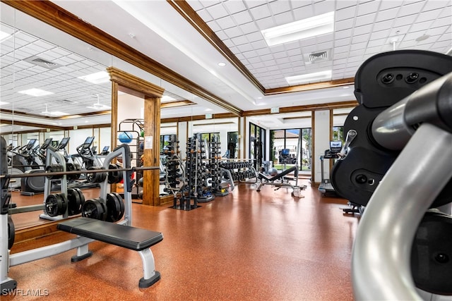 exercise room with a paneled ceiling, ornamental molding, and a raised ceiling