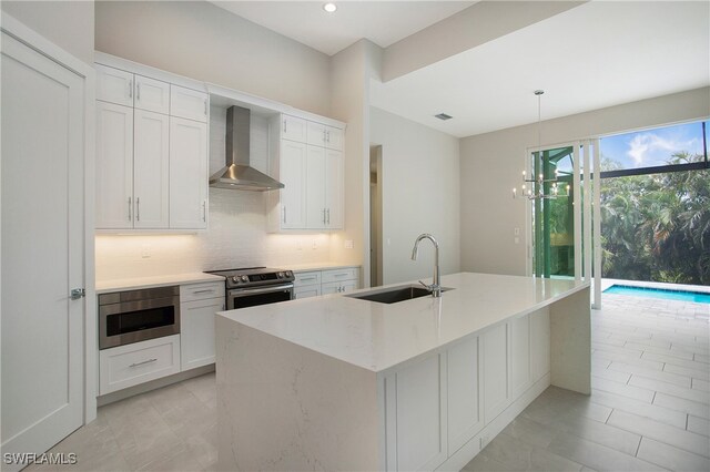 kitchen featuring white cabinetry, sink, appliances with stainless steel finishes, wall chimney exhaust hood, and hanging light fixtures