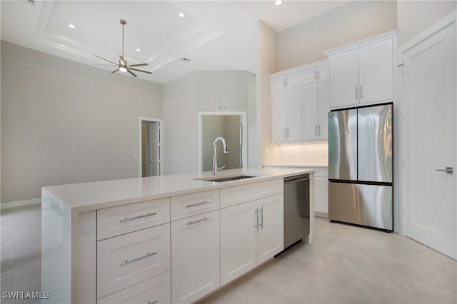 kitchen featuring stainless steel appliances, white cabinets, a raised ceiling, and a center island with sink