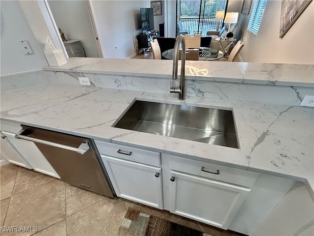 kitchen featuring light tile patterned flooring, sink, light stone countertops, stainless steel dishwasher, and white cabinets