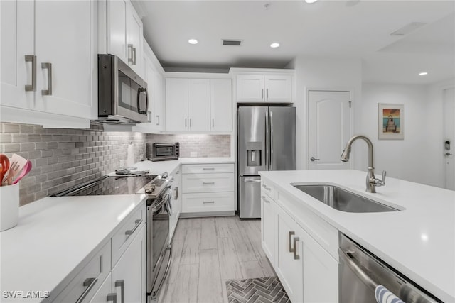 kitchen featuring stainless steel appliances, white cabinetry, sink, light hardwood / wood-style flooring, and decorative backsplash