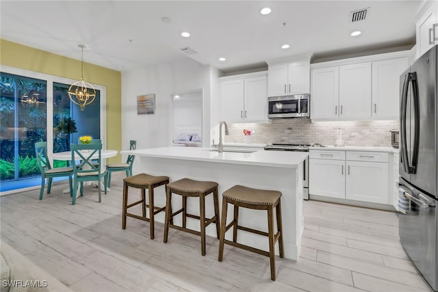 kitchen with pendant lighting, appliances with stainless steel finishes, white cabinets, and an island with sink