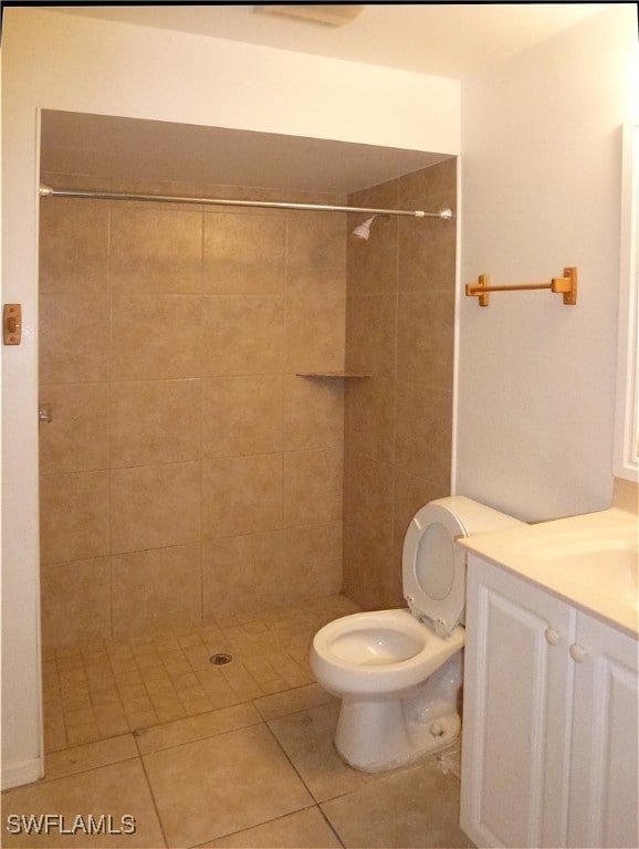 bathroom featuring toilet, tile patterned flooring, vanity, and a tile shower