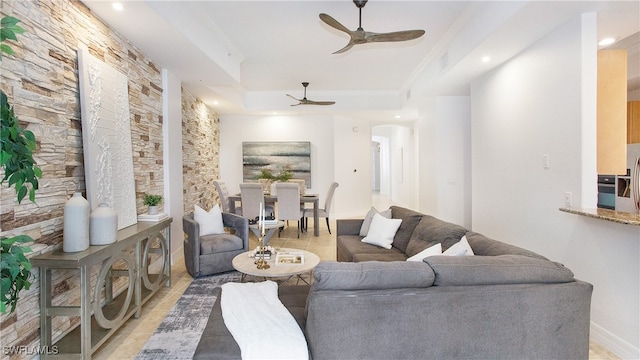 living room featuring light tile patterned floors, ceiling fan, a raised ceiling, and ornamental molding