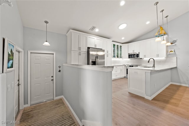 kitchen featuring white cabinetry, kitchen peninsula, decorative light fixtures, vaulted ceiling, and appliances with stainless steel finishes