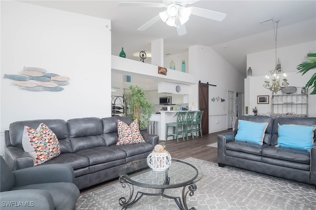 living room with high vaulted ceiling, a barn door, hardwood / wood-style flooring, and ceiling fan with notable chandelier