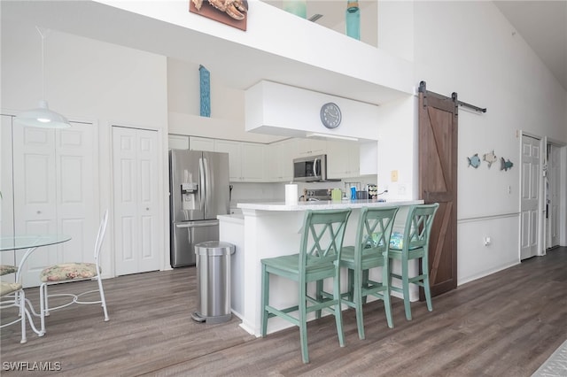 kitchen with stainless steel appliances, white cabinetry, a barn door, high vaulted ceiling, and kitchen peninsula