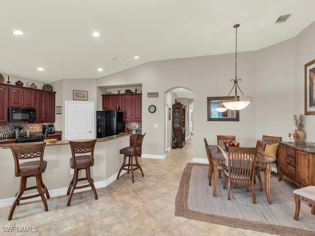 kitchen featuring a breakfast bar, lofted ceiling, backsplash, black appliances, and light tile patterned flooring