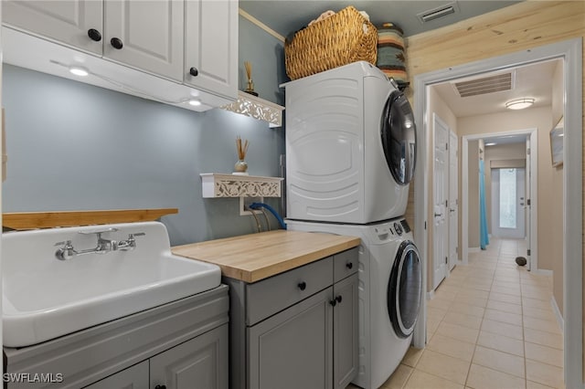 clothes washing area with stacked washer / drying machine, cabinets, light tile patterned floors, and sink