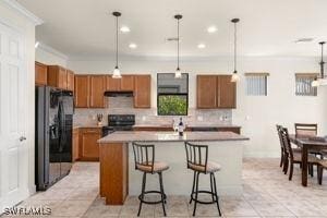 kitchen with a kitchen island with sink, a kitchen breakfast bar, hanging light fixtures, brown cabinets, and black appliances