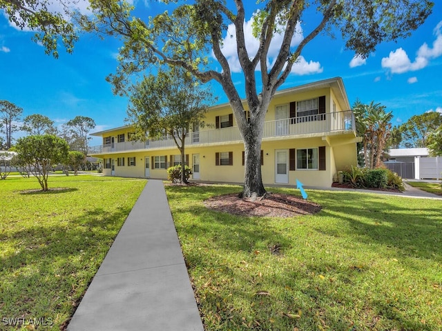 view of front of property with a balcony, a front yard, and central AC