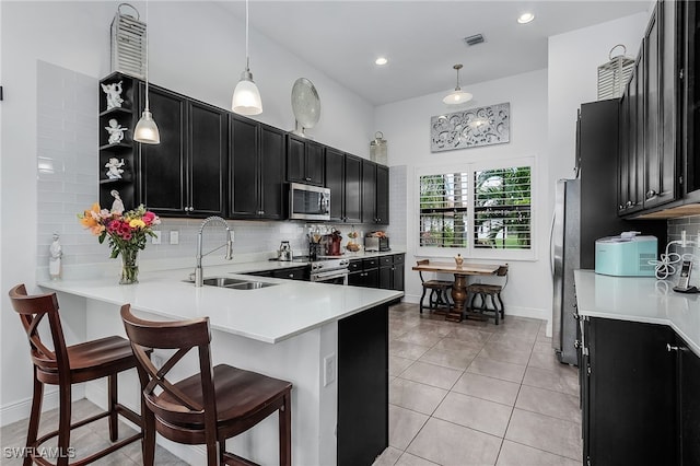 kitchen with sink, appliances with stainless steel finishes, decorative light fixtures, kitchen peninsula, and a breakfast bar area