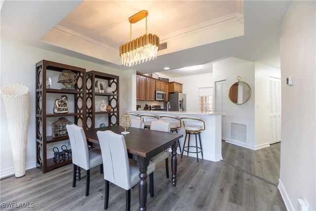 dining room with crown molding, a chandelier, hardwood / wood-style flooring, and a raised ceiling