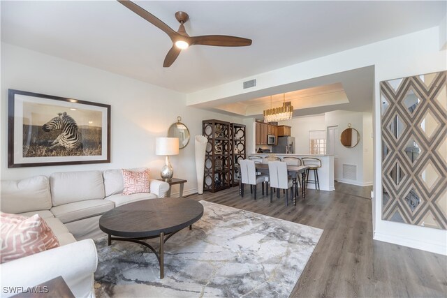 living room with hardwood / wood-style flooring, ceiling fan with notable chandelier, and a tray ceiling