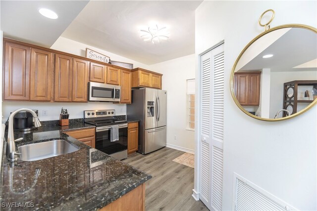 kitchen with dark stone countertops, appliances with stainless steel finishes, sink, and light hardwood / wood-style flooring