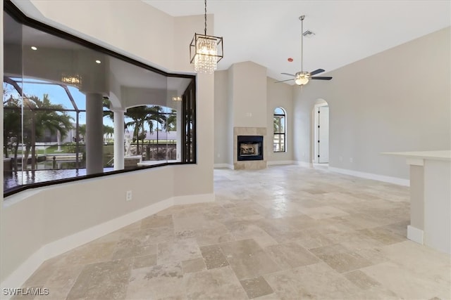 interior space featuring a tiled fireplace, a towering ceiling, a healthy amount of sunlight, and ceiling fan with notable chandelier