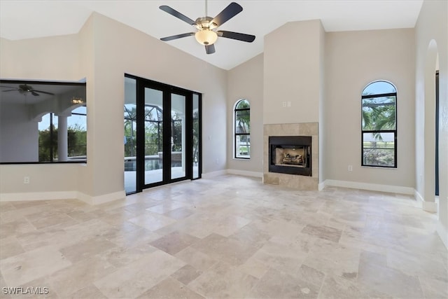 unfurnished living room with a tile fireplace, a wealth of natural light, and a high ceiling