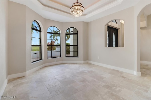 empty room featuring a tray ceiling, ornamental molding, and a notable chandelier