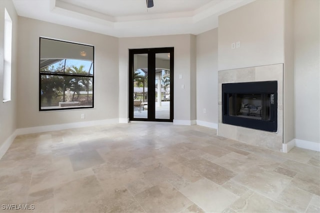 unfurnished living room with ceiling fan, a raised ceiling, and a fireplace