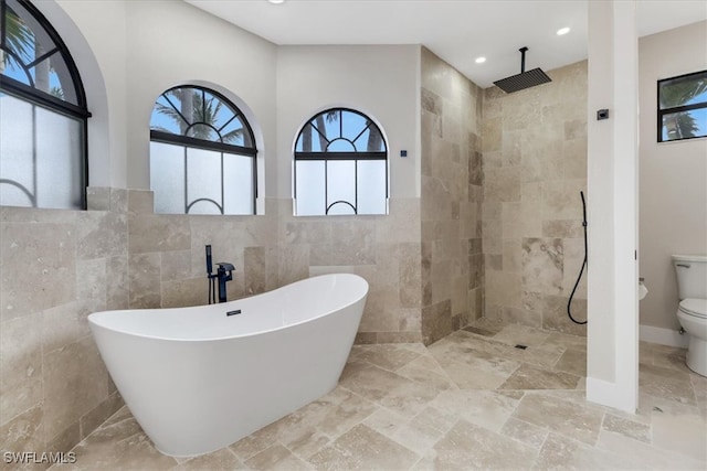 bathroom featuring separate shower and tub, toilet, and tile walls