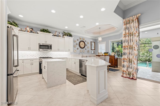 kitchen featuring kitchen peninsula, crown molding, a kitchen island, appliances with stainless steel finishes, and decorative light fixtures