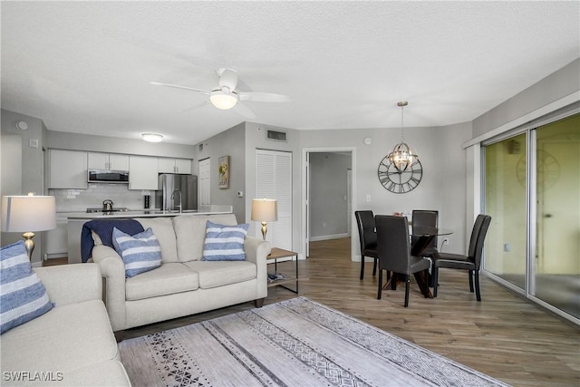 living room featuring sink, hardwood / wood-style flooring, ceiling fan with notable chandelier, and a textured ceiling