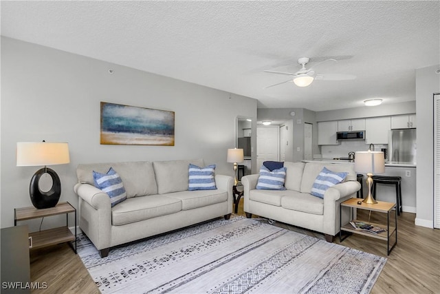 living room with ceiling fan, light hardwood / wood-style floors, and a textured ceiling